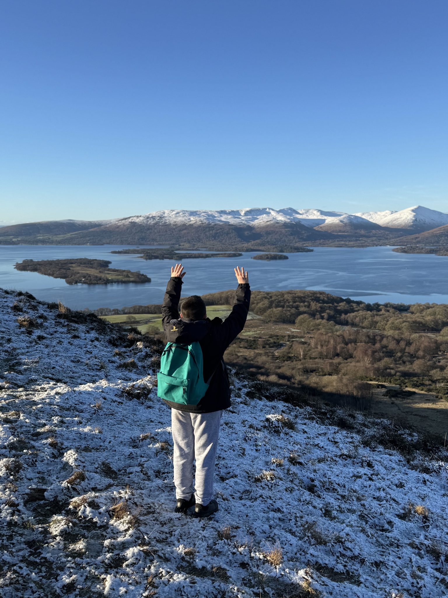 Young boy on conic hill raising arms in the air